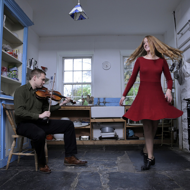 Ciaran playing fiddle and Caitlín Nic Gabhann dancing on flagstone kitchen