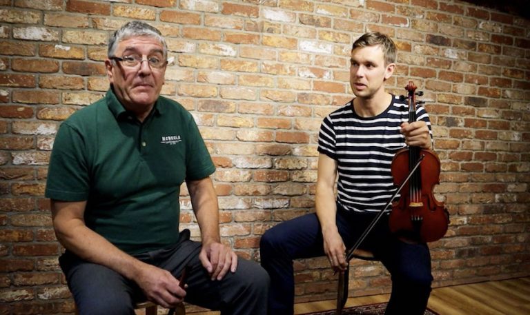 Paraic McNeela and Liam O'Connor sitting in the McNeela Instruments Studio with whistle and fiddle/violin ready to play the Kesh Jig
